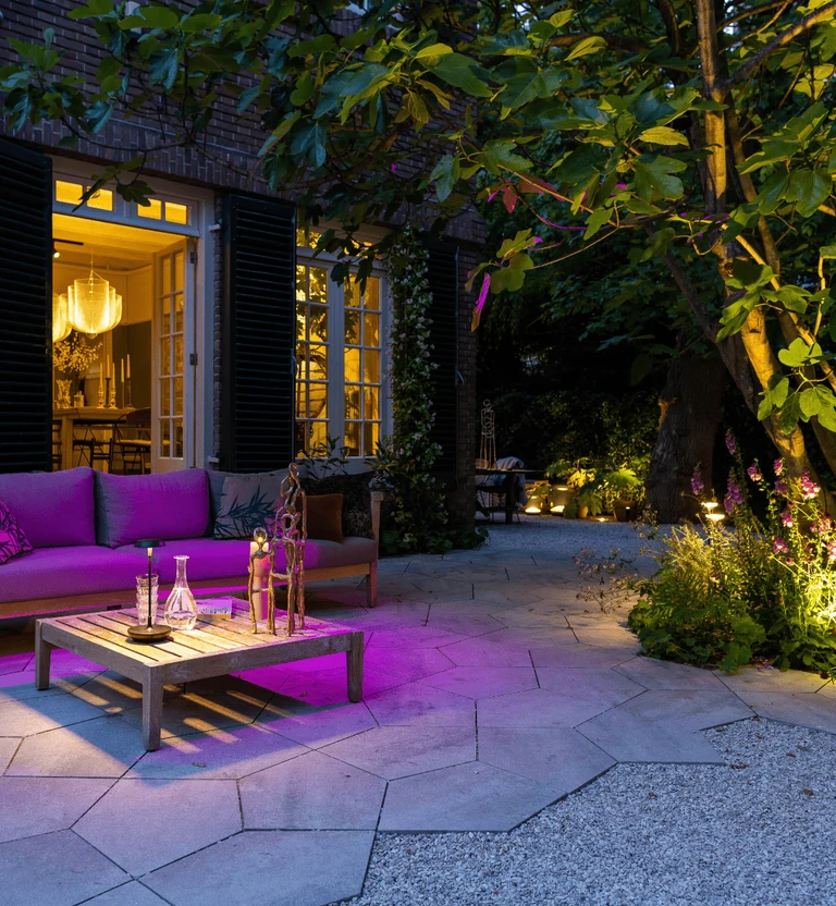 Loungehoek in een in-lite tuin met warm wit en paars accentlicht