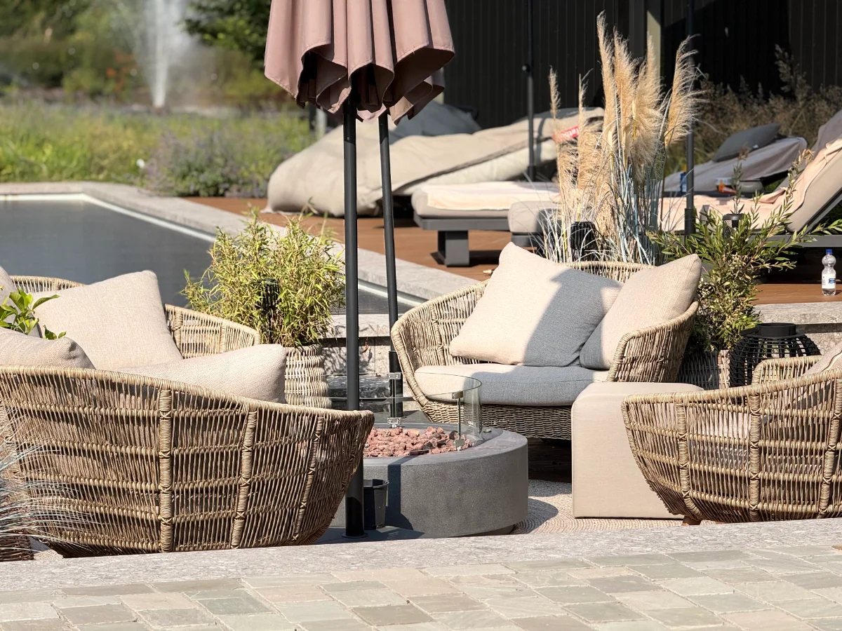 Zithoek met geweven loungestoelen, siergrassen en bestrating naast een zwembad
