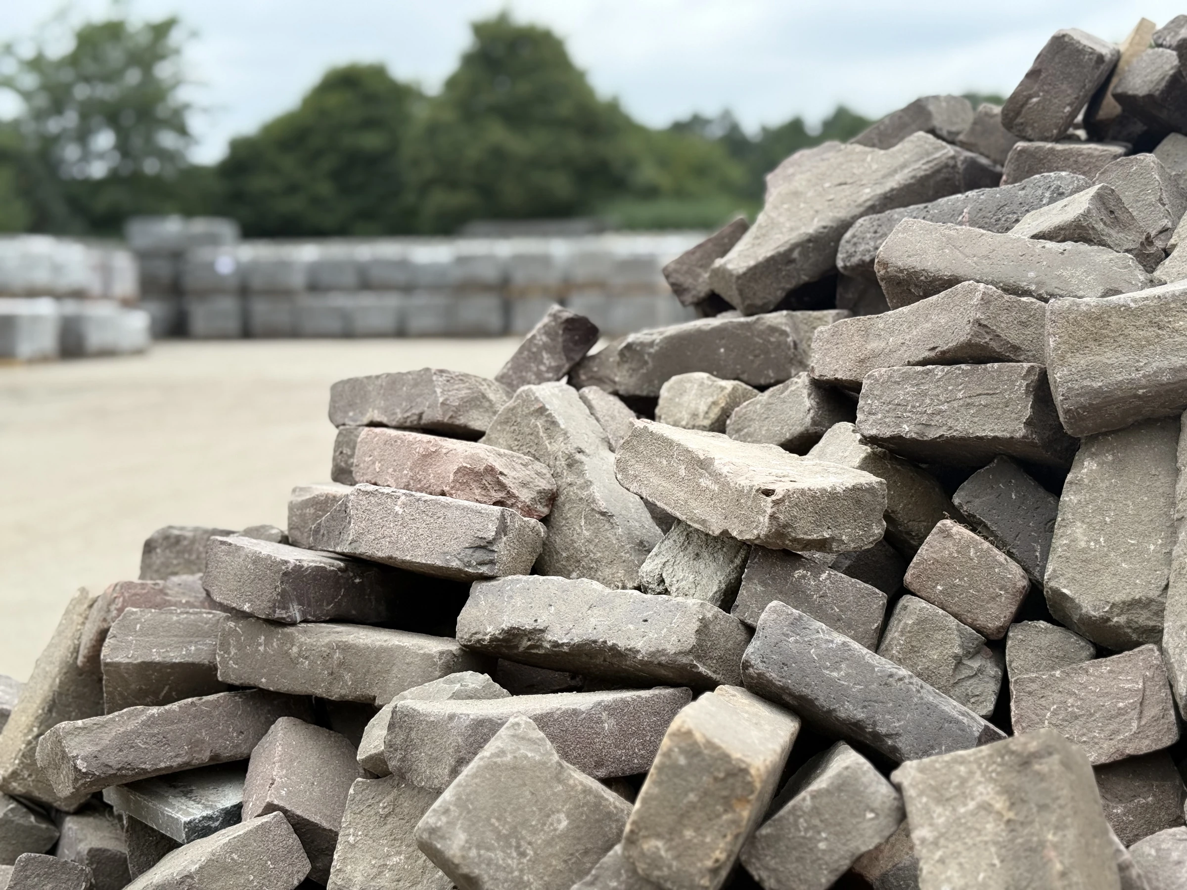Een stapel verweerde klinkers met verpakte pallets op de achtergrond.