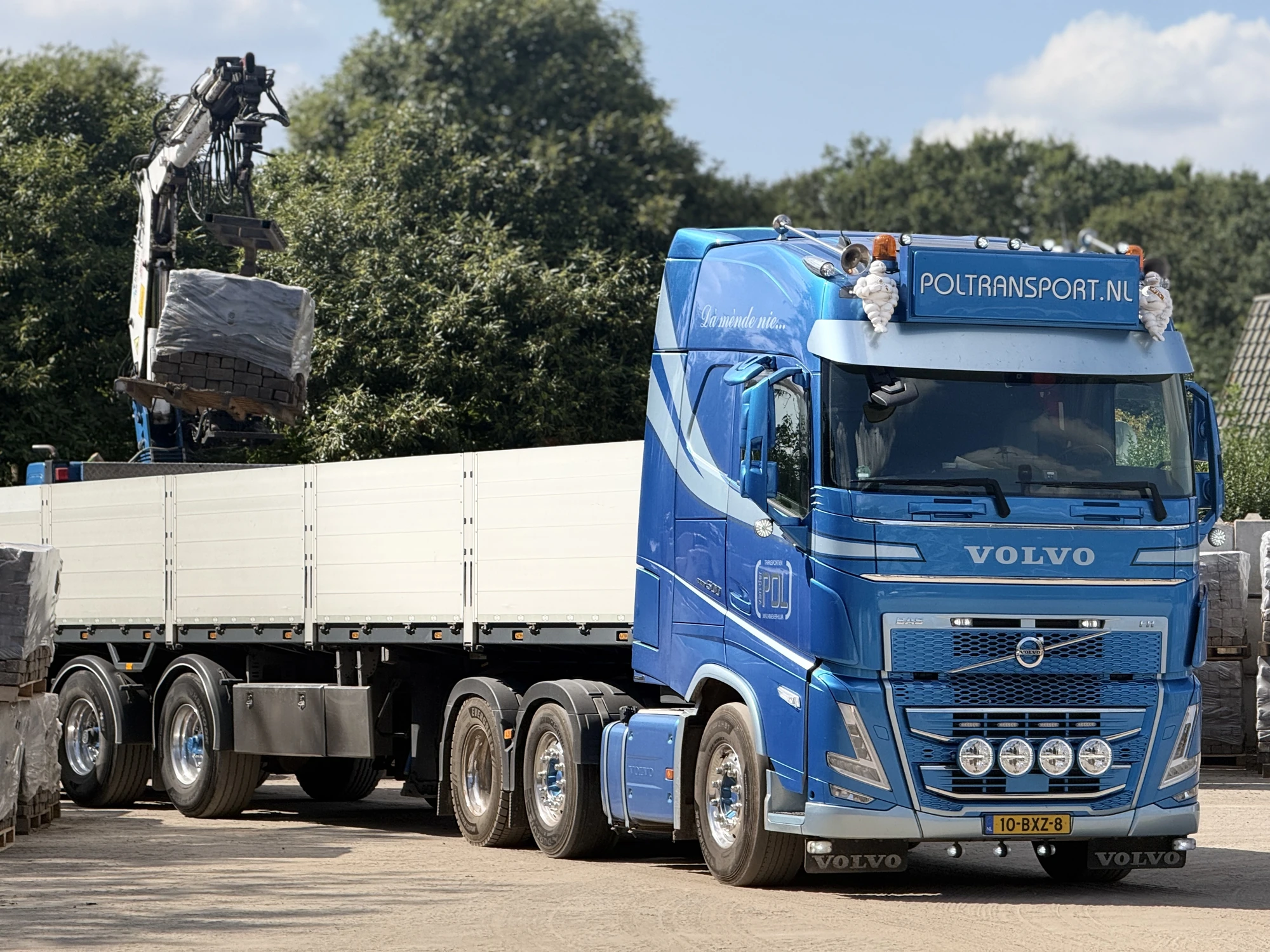 Een kraan houdt een verpakte pallet met klinkers boven een vrachtwagen.